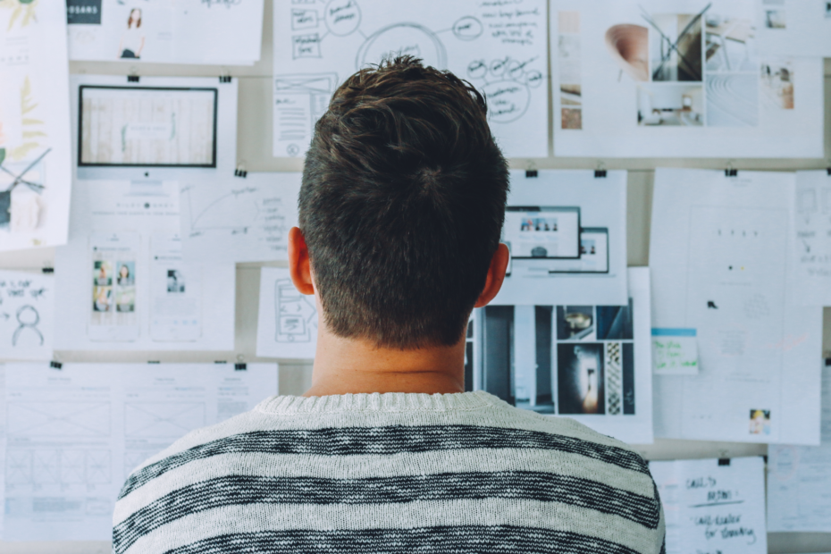 A man viewing a board of planning tools, featuring graphs, diagrams, research, and statistics, from behind.