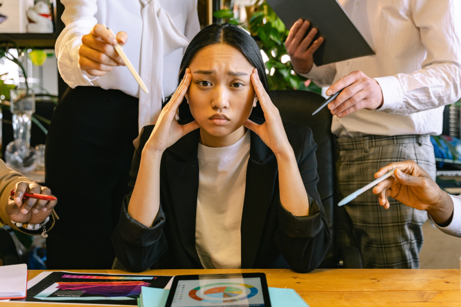 A stressed-out girl sitting at a desk with hands up to temples, wearing an expression of overwhelm.