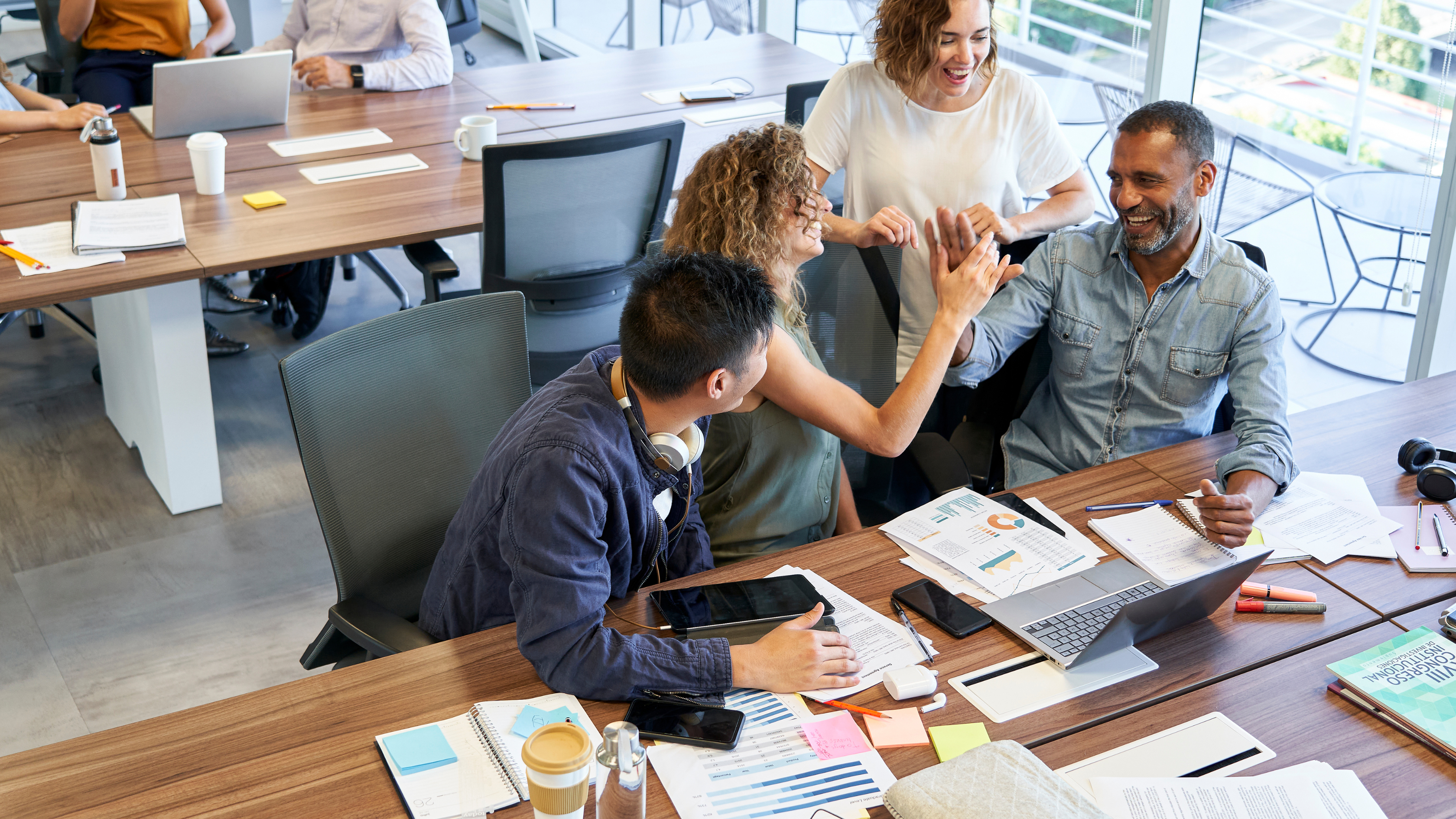 Four individuals engaged in a conversation at a desk in an office setting.