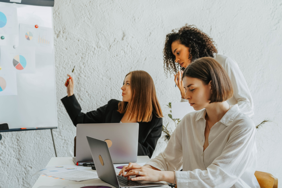 Three diverse women focused on a whiteboard with graphs in an office.