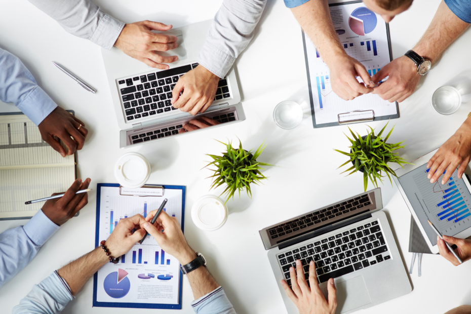 Top-down view of six pairs of hands working on computers in a diverse office setting.