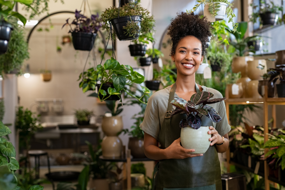 Woman of color business owner holding a plant, surrounded by plants.