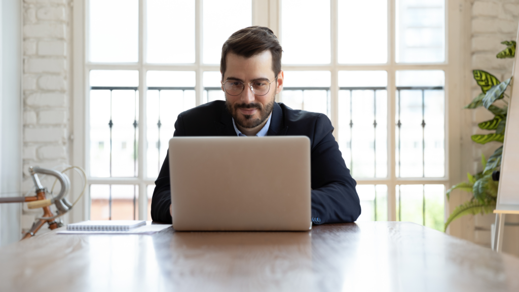 A business man with glasses sitting at a desk with a computer, focused on work.