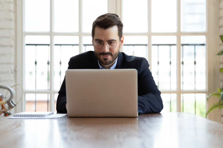 A business man with glasses sitting at a desk with a computer, focused on work.