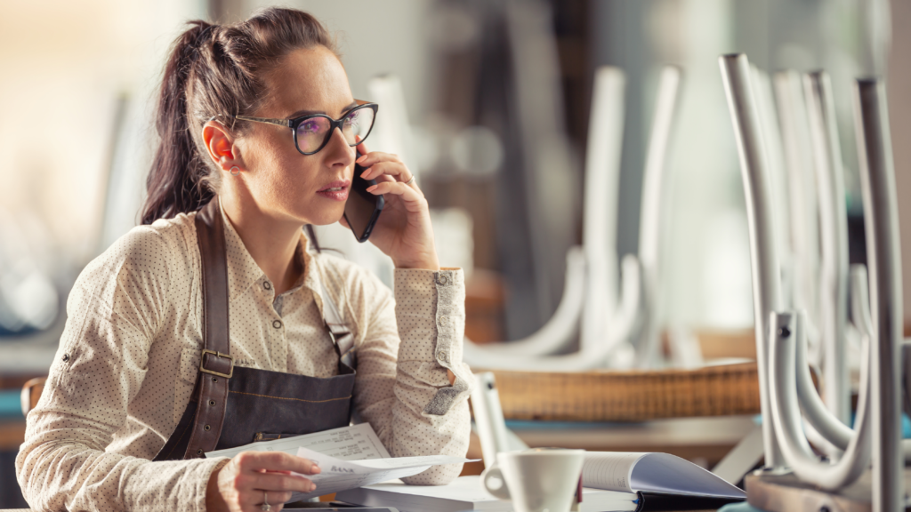 A business owner with glasses sitting at a desk, talking on the phone.