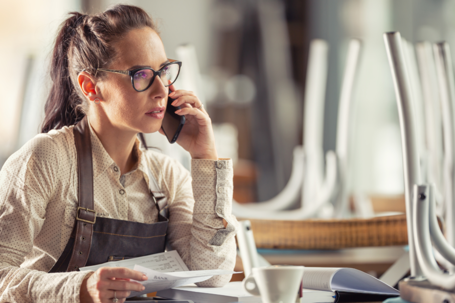 A business owner with glasses sitting at a desk, talking on the phone.