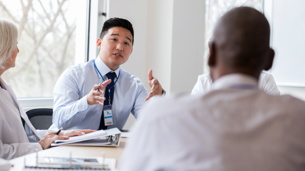 A confident man sitting at a modern conference table in a well-lit office, passionately delivering a pitch to a small audience.