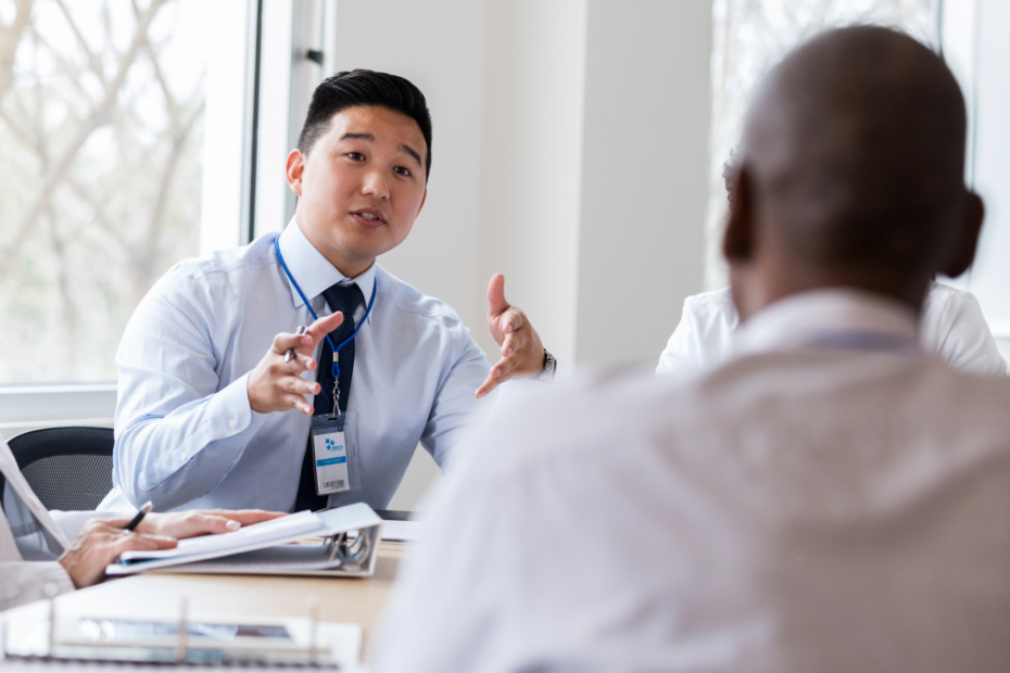 A confident man sitting at a modern conference table in a well-lit office, passionately delivering a pitch to a small audience.
