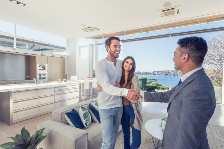 A real estate agent shaking hands with a smiling couple in a well-appointed kitchen, sealing a deal on a new home.