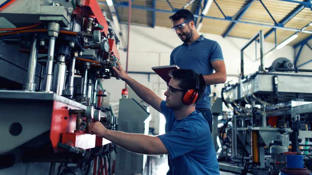 Two men in goggles working at a manufacturing plant, fixing a machine.