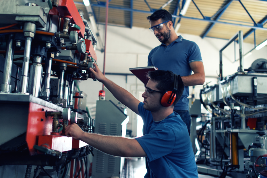 Two men in goggles working at a manufacturing plant, fixing a machine.