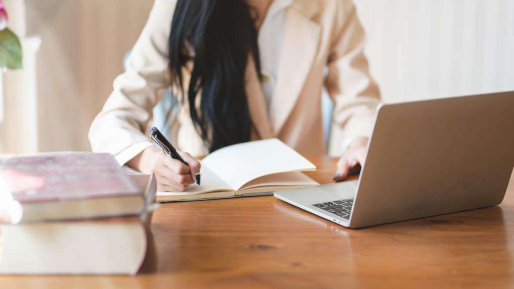 A business woman is evaluating her loan options on the laptop while sitting at a desk with a notepad.