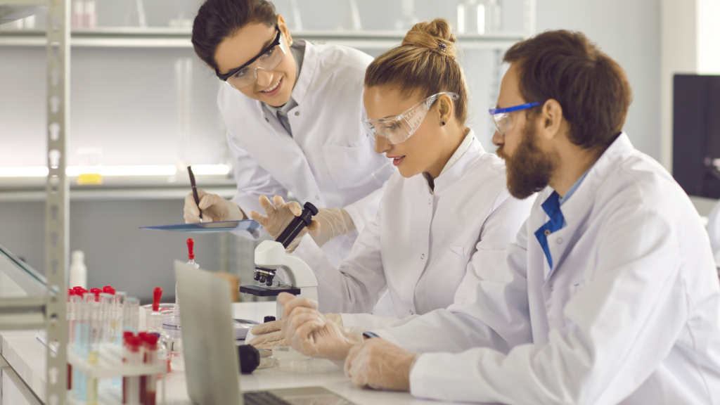 Three colleagues working at a lab in white coats with a microscope.