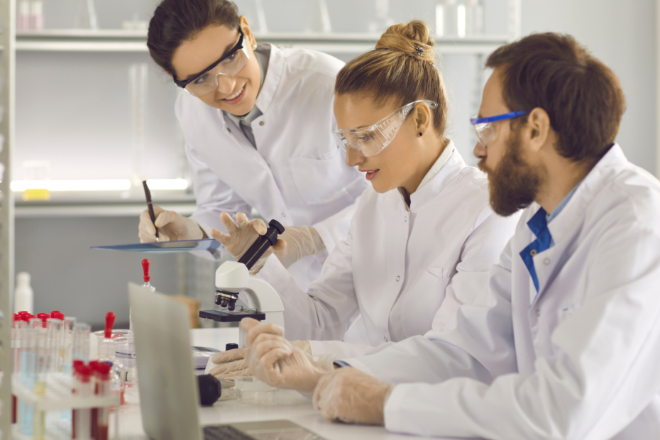 Three colleagues working at a lab in white coats with a microscope.